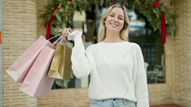 Młoda Blondynka Uśmiecha Się Idąc Zakupy Trzymając Torby Ulicy — Wideo stockowe