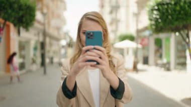 Genç sarışın kadın gülümsüyor. Kendine güveniyor. Akıllı telefonun yanında fotoğraf çekiyor.