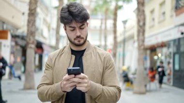 Genç İspanyol adam akıllı telefon kullanıyor. Sokakta ciddi bir ifadesi var.
