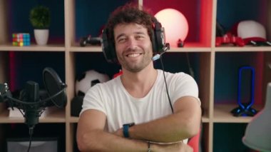 Young hispanic man streamer smiling confident sitting with arms crossed gesture at music studio