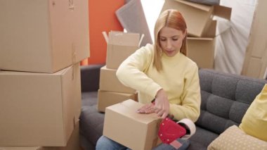 Genç sarışın kadın yeni evinde kendine güvenen bir karton kutu paketliyor.