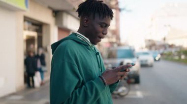 Sokakta akıllı telefon kullanan, kendinden emin gülümseyen Afrikalı Amerikalı bir adam.