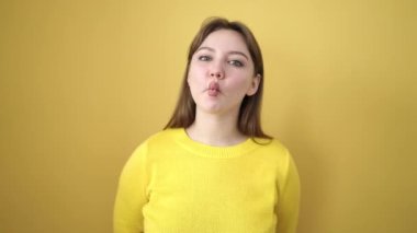 Sarışın genç kadın, izole edilmiş sarı arka planda dudakları olan komik bir jest yapıyor.