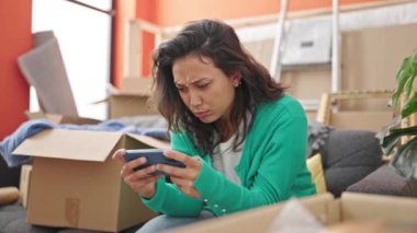 Yeni evindeki kanepede oturmuş video oyunu oynayan genç ve güzel İspanyol kadın.