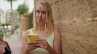 Sokakta akıllı telefon kullanan, kendine güvenen genç sarışın kadın.