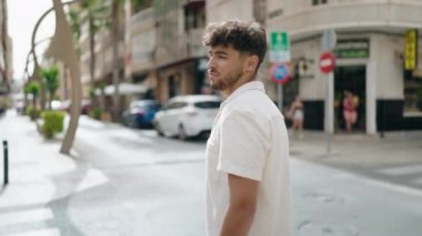 Genç Arap adam gülümsüyor. Kollarını kavuşturup caddede duruyor.