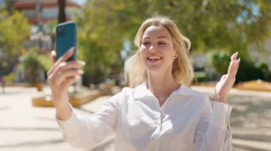Young blonde woman smiling confident having video call at park