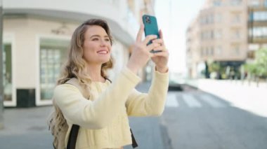 Sarışın genç bir kadın turist sokakta akıllı telefonun yanında fotoğraf çekiyor.