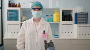 Laboratuvarda bilim adamı üniforması ve tıbbi maske giyen genç sarışın kadın.