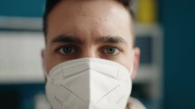 Laboratuvarda bilim adamı üniforması ve tıbbi maske giyen genç İspanyol adam.