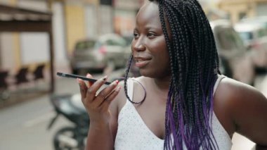 Afro-Amerikalı kadın gülümsüyor. Akıllı telefondan konuşuyor.