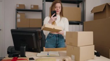 Genç sarışın kadın ecommerce iş çalışanı ofiste akıllı telefon kullanarak paket tarama