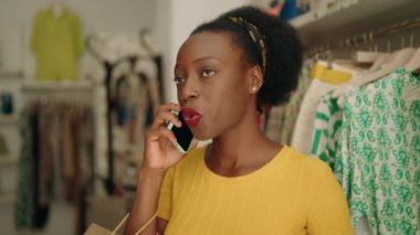 African american woman customer holding shopping bags talking on smartphone at clothing store