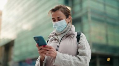 Sokaklarda akıllı telefon kullanan orta yaşlı kadın tıbbi maske takıyor.