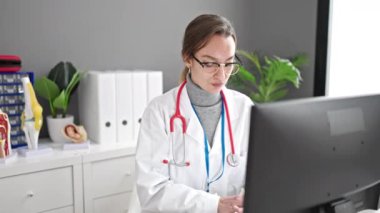 Genç beyaz kadın doktor klinikte bilgisayar kullanıyor.