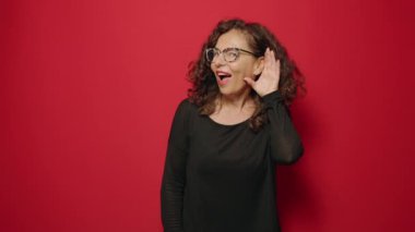 Orta yaşlı, kendine güvenen bir kadın kırmızı arka planda jest yapıyor.