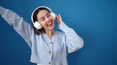 Young beautiful hispanic woman smiling confident listening to music dancing over isolated blue background