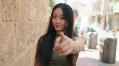 Genç Çinli kadın gülümsüyor. Kendinden emin. Sokakta el kol hareketi yapıyor.