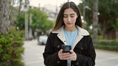 Parkta akıllı telefon kullanarak gülümseyen güzel bir İspanyol kadın.
