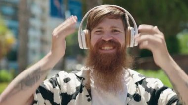 Genç kızıl saçlı adam parkta müzik dinliyor ve dans ediyor.