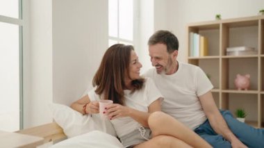 Man and woman couple drinking coffee sitting on bed at bedroom