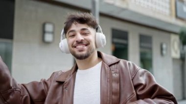 Genç Arap adam kendinden emin bir şekilde gülümsüyor müzik dinliyor ve sokakta dans ediyor.