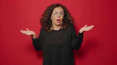 Kırmızı arka planda duran şüpheci orta yaşlı bir kadın.