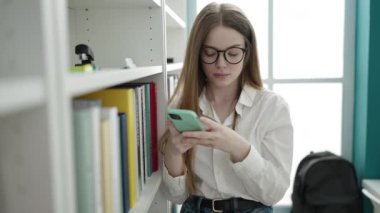 Young blonde woman student using smartphone at university classroom