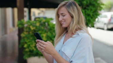 Sokakta akıllı telefon kullanan, kendine güvenen genç sarışın kadın.