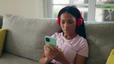 Afro-Amerikalı kadın evdeki kanepede oturmuş müzik dinliyor.