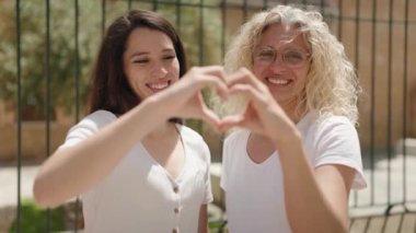 İki kadın, anne ve kız, sokakta kalp hareketi yapıyorlar.