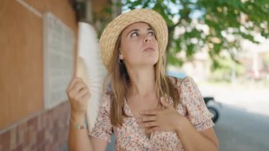 Sokakta pervane kullanan yaz şapkası takan genç bir kadın turist.