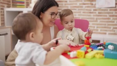 Anaokulunda masada oturan, çocuklarla oynayan bir öğretmen.