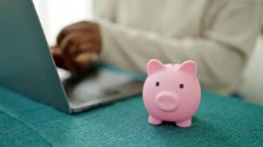 Afro-Amerikalı kadın yemek odasında domuz kumbarasına para yerleştiriyor.