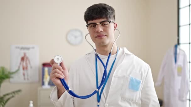 年轻的惊慌失措的医生面带微笑 自信地在诊所举着听诊器 — 图库视频影像