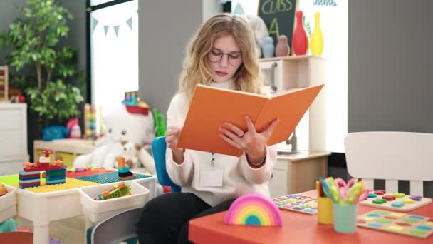 Young Blonde Woman Preschool Teacher Reading Book Relaxed Expression Kindergarten — Video Stock