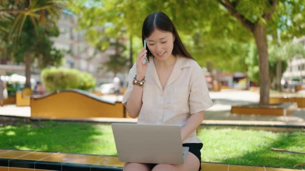 中国妇女在公园用笔记本电脑在智能手机上交谈 — 图库视频影像
