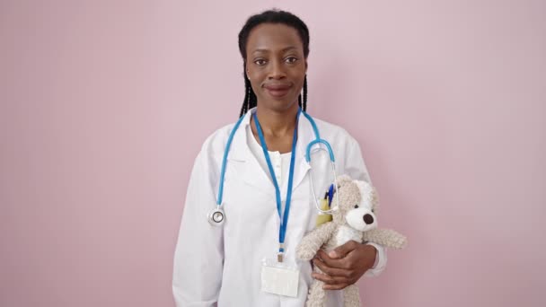 Mujer Afroamericana Doctora Sonriendo Confiada Sosteniendo Oso Peluche Sobre Fondo — Vídeos de Stock