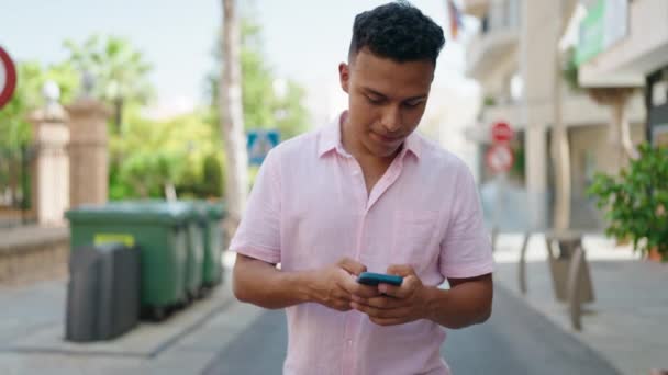 Joven Latino Sonriendo Confiado Usando Smartphone Caminando Por Calle — Vídeo de stock