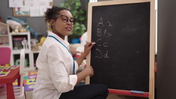 African American Woman Teacher Smiling Confident Writing Blackboard Kindergarten — Video