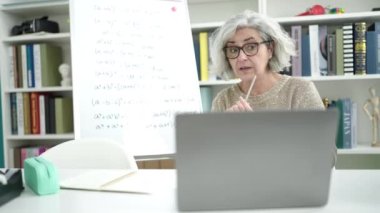 Middle age woman with grey hair teacher teaching online maths lesson at university classroom