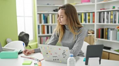 Kütüphane üniversitesinde dizüstü bilgisayar ve dokunmatik kağıt kullanan beyaz bir kız öğrenci.