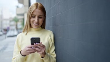 Sokakta akıllı telefon kullanan, kendine güvenen genç sarışın kadın.