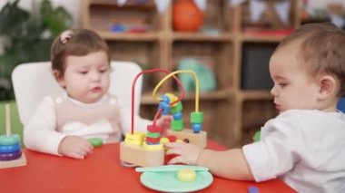 Anaokulunda masada oturmuş oyuncaklarla oynayan iki çocuk.