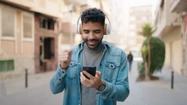Genç Arap adam kendinden emin bir şekilde gülerek sokakta müzik dinliyor.