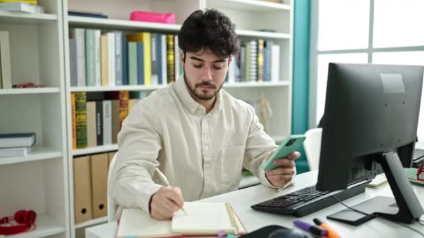 Jovem Estudante Hispânico Usando Computador Smartphone Escrevendo Notas Universidade Biblioteca — Vídeo de Stock