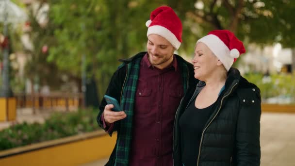 母と息子の身に着けているクリスマスの帽子作ります自画撮りスマートフォンによって公園 — ストック動画