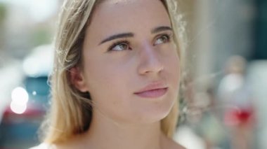 Sokakta ciddi bir ifadeyle gökyüzüne bakan genç sarışın kadın.