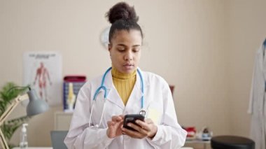 Genç Afrikalı Amerikalı kadın doktor klinikte akıllı telefon kullanıyor.