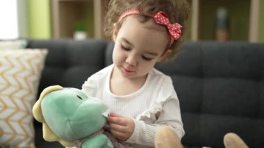 Evdeki kanepede oturan sevimli beyaz kız bebeklerle oynuyor.